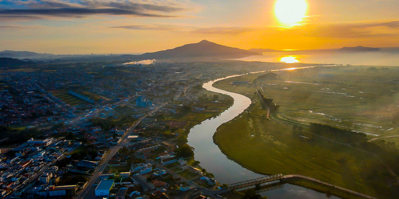 Vista aérea de Tijucas com o rio e a montanha ao pôr do sol